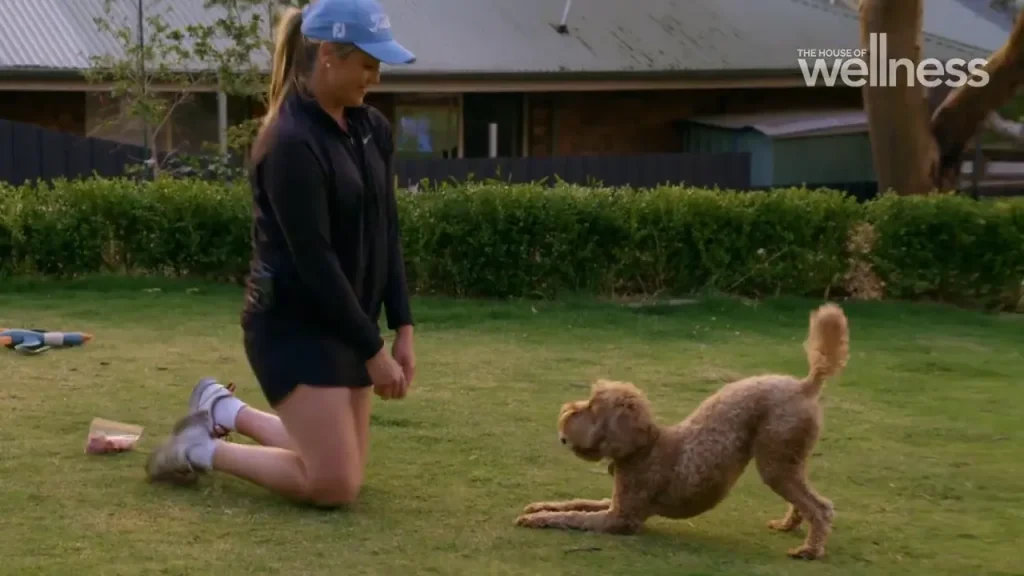 Woman kneeling and smiling at a playful dog in a backyard garden.